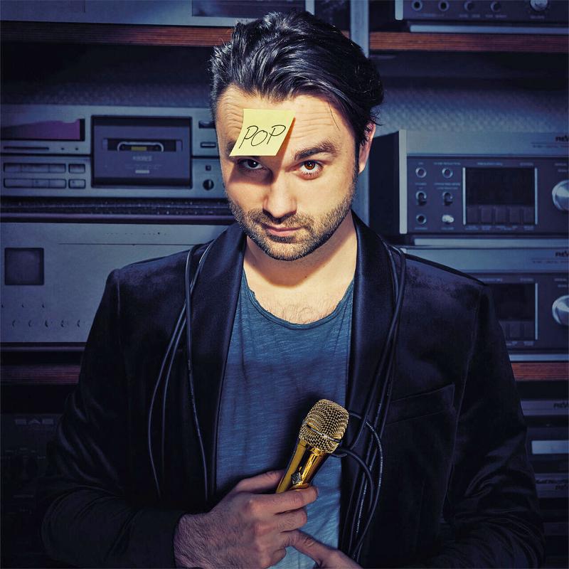 Portraitbild von einem Mann mit einem Zettel "Pop" auf der Stirn.